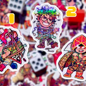 May include: Set of three holographic stickers featuring cartoon characters. One sticker shows a character with a red hat and wrapped in a bundle. Another shows a character wrapped in strings. The third shows a character with a dice-shaped hat.