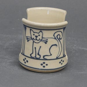 May include: A ceramic dish soap dispenser with a blue and white cat design. The dispenser is off-white with a blue cat design and blue dots around the bottom.