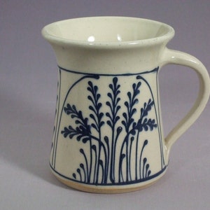 May include: A white ceramic mug with a blue floral design. The mug has a wide base and a flared rim.