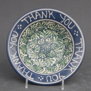 May include: A blue and white ceramic bowl with a green floral design. The bowl has the words "Thank You" written around the rim.