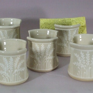 May include: Five beige ceramic soap dishes with a white floral design. The dishes are arranged in a semi-circle on a light gray surface.