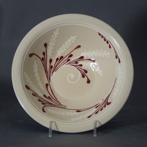 May include: A beige ceramic bowl with a swirling design of white and burgundy lines. The bowl has a slightly raised rim.