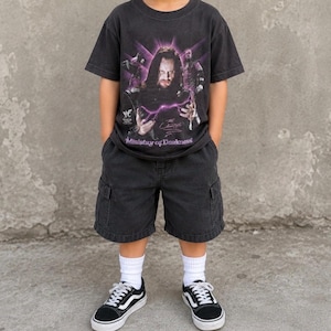 May include: A black short-sleeve t-shirt featuring a graphic print of The Undertaker with purple lightning effects and the text Ministry of Darkness, paired with black cargo shorts, white crew socks, and black and white low-top sneakers.