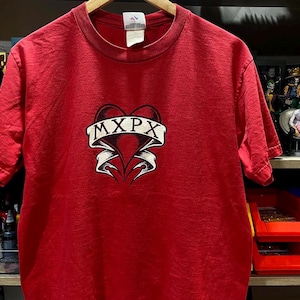 Peut inclure: T-shirt rouge avec un cœur noir et le texte "MXPX" sur une bannière blanche.