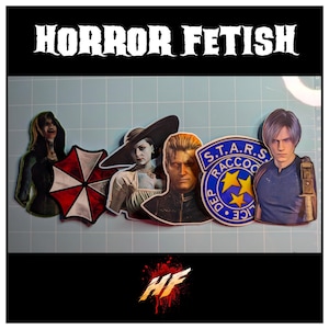 May include: A collection of six Resident Evil themed stickers featuring characters and symbols including the Umbrella Corporation logo, a S.T.A.R.S. Raccoon Police Department badge, and various figures, all displayed on a grid mat with the text HORROR FETISH.