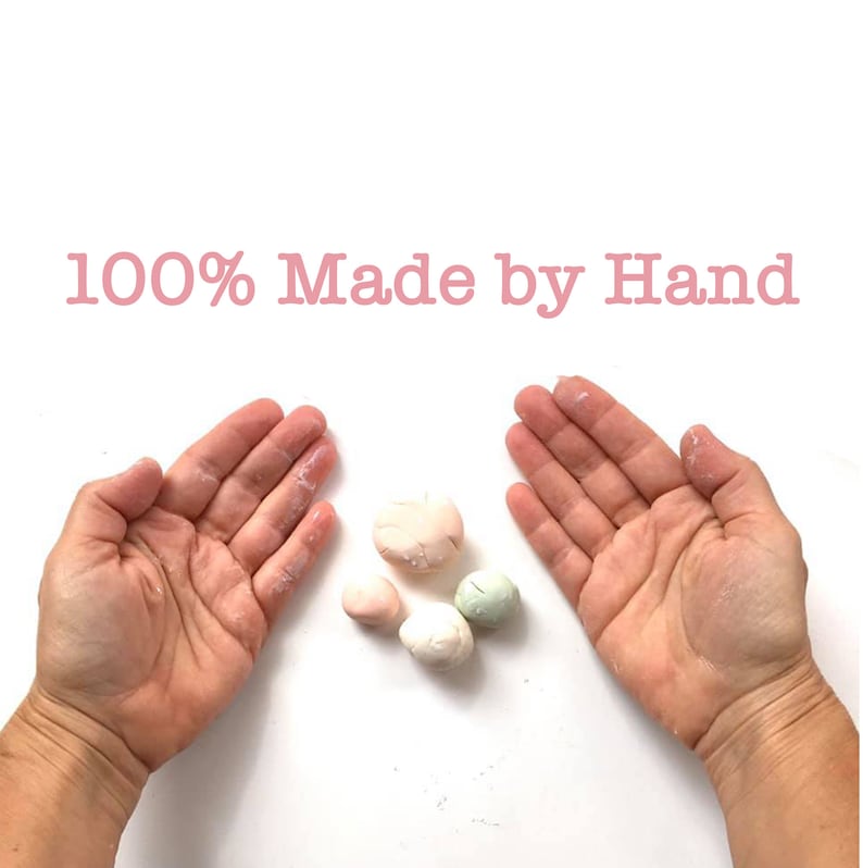 May include: Close-up of two hands with a small pile of four handmade, pastel-colored clay balls in the center. The text "100% Made by Hand" is at the top of the image.