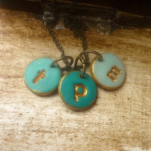 May include: A turquoise and gold necklace with three round charms. Each charm has a gold letter on it: T, P, and M.