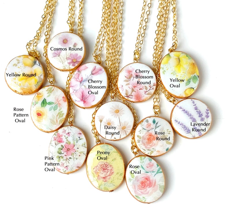 May include: A collection of 10 floral-themed necklaces with gold chains. The pendants are round and oval, featuring various floral designs, including roses, daisies, cherry blossoms, and lavender. Each pendant has a different floral name and shape written on it.