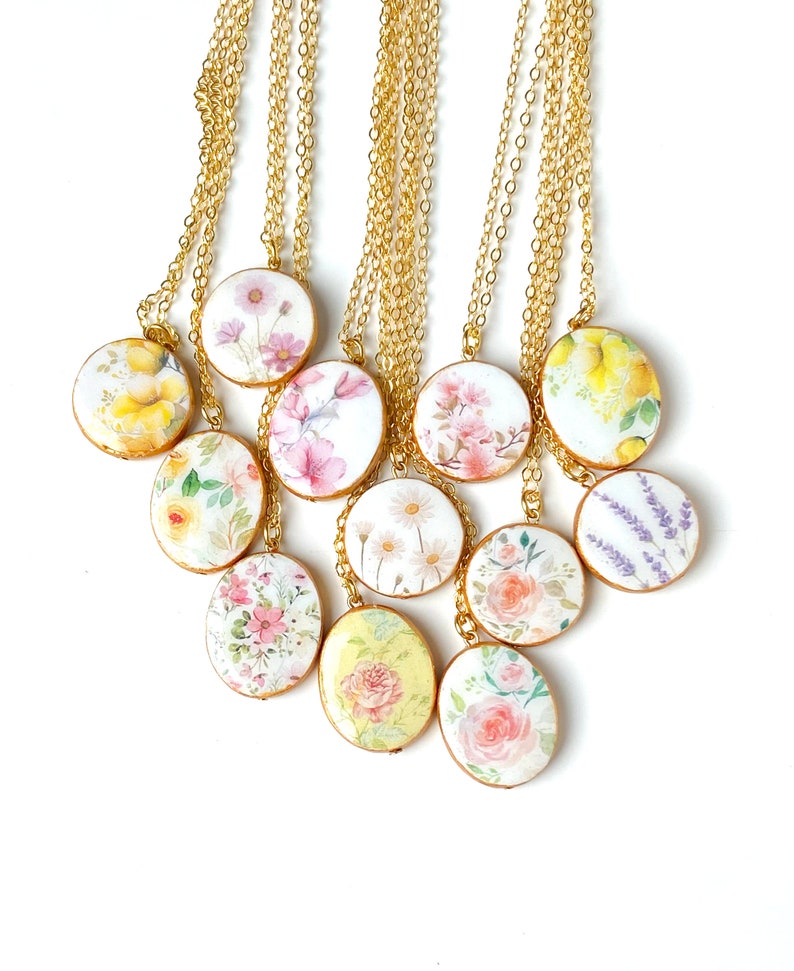 May include: A set of 10 gold chain necklaces with oval-shaped pendants featuring different floral patterns. The pendants are white with watercolour-style floral designs in shades of pink, yellow, and purple.