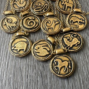 May include: Gold-colored pendant necklaces featuring zodiac animal symbols. Each circular pendant has a black border and a gold-colored animal design. The necklaces are on gold chains.