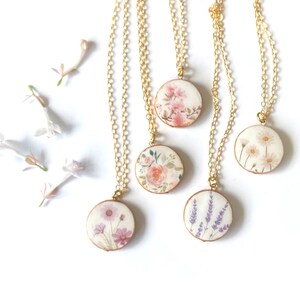 May include: Five gold chain necklaces with round pendants featuring pressed flower designs. The pendants feature different floral patterns, including pink roses, lavender, daisies, and cosmos.