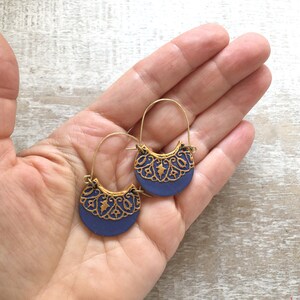 May include: A pair of gold hoop earrings with a blue half-circle pendant. The pendant has a gold filigree design.