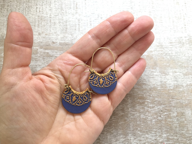 May include: A pair of gold hoop earrings with a blue half-circle pendant. The pendant has a gold filigree design.