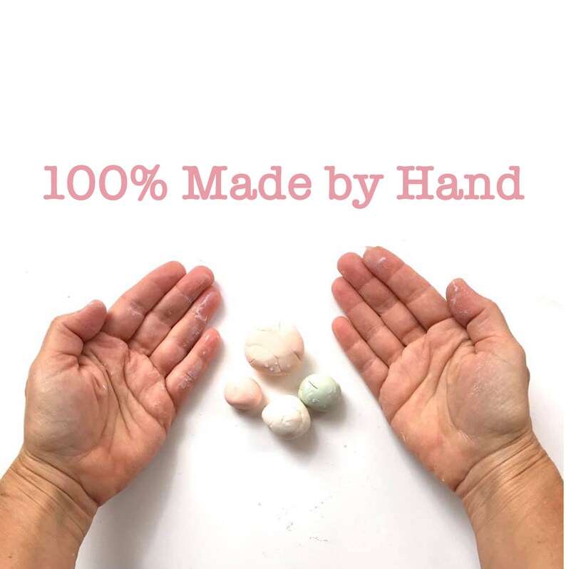 May include: Close-up of two hands with a small pile of four handmade, pastel-colored clay balls in the center. The text "100% Made by Hand" is at the top of the image.