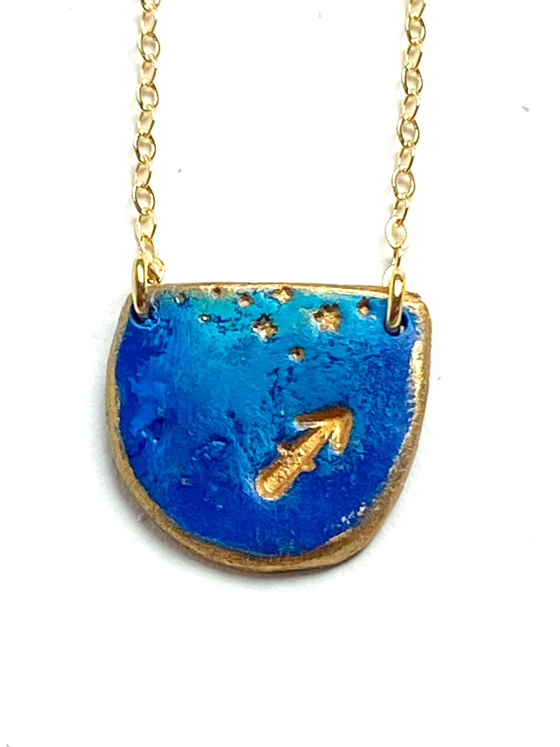 K&ouml;nnte beinhalten: Goldkette mit einem blauen und goldenen Anh&auml;nger mit dem Sternzeichen Sch&uuml;tze.