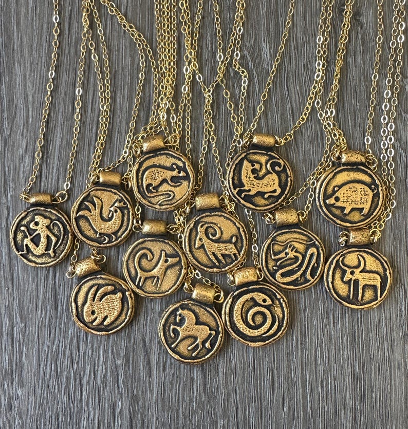 May include: Gold-colored pendant necklaces with zodiac symbols. Each pendant features a different animal design, including a rat, rooster, and rabbit, on a circular base. The necklaces have delicate gold chains.