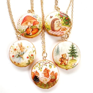 May include: Five round pendants on gold-tone chains, each featuring a different illustration: a fox sleeping under a mushroom, a hedgehog having tea, a rabbit holding flowers, three squirrels at a table, and a bear walking in a forest.