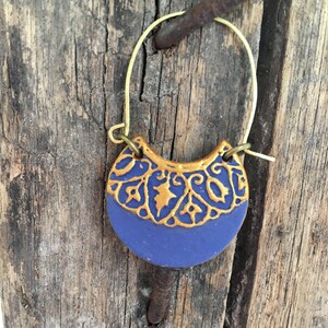 May include: A pair of gold hoop earrings with a blue and gold ceramic crescent moon pendant. The pendant features a gold filigree design.