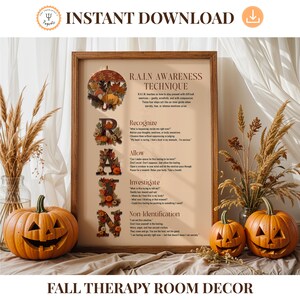 May include: A framed print with the text "R.A.I.N. Awareness Technique" and the word "FALL" decorated with fall foliage. Two carved pumpkins and decorative grasses flank the print. The words "Fall Therapy Room Decor" are at the bottom.