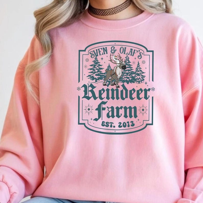 May include: Pink sweatshirt with a graphic featuring the text "Sven & Olaf's Reindeer Farm EST. 2013". The design includes a reindeer, pine trees, and decorative elements. The sweatshirt is a solid pink color.