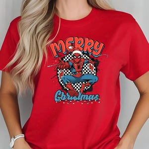 Puede incluir: Camiseta roja con un dise&ntilde;o de Spider-Man con gorro de Pap&aacute; Noel, con las palabras "Merry Christmas" y "Christmas". El dise&ntilde;o incluye un fondo a cuadros y detalles coloridos.