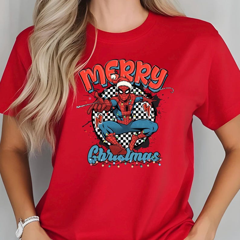 Puede incluir: Camiseta roja con un dise&ntilde;o de Spider-Man con gorro de Pap&aacute; Noel, con las palabras "Merry Christmas" y "Christmas". El dise&ntilde;o incluye un fondo a cuadros y detalles coloridos.