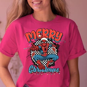 Puede incluir: Camiseta magenta con un dise&ntilde;o festivo de Spider-Man con un gorro de Pap&aacute; Noel, con las palabras "Merry Christmas". El dise&ntilde;o incluye un fondo a cuadros y luces navide&ntilde;as, creando un tema navide&ntilde;o.