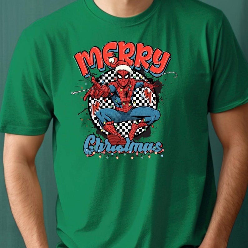 Puede incluir: Camiseta verde con un gr&aacute;fico de Spider-Man con un gorro de Pap&aacute; Noel y las palabras "Merry Christmas" en rojo y azul. El superh&eacute;roe est&aacute; sobre un fondo a cuadros en blanco y negro.