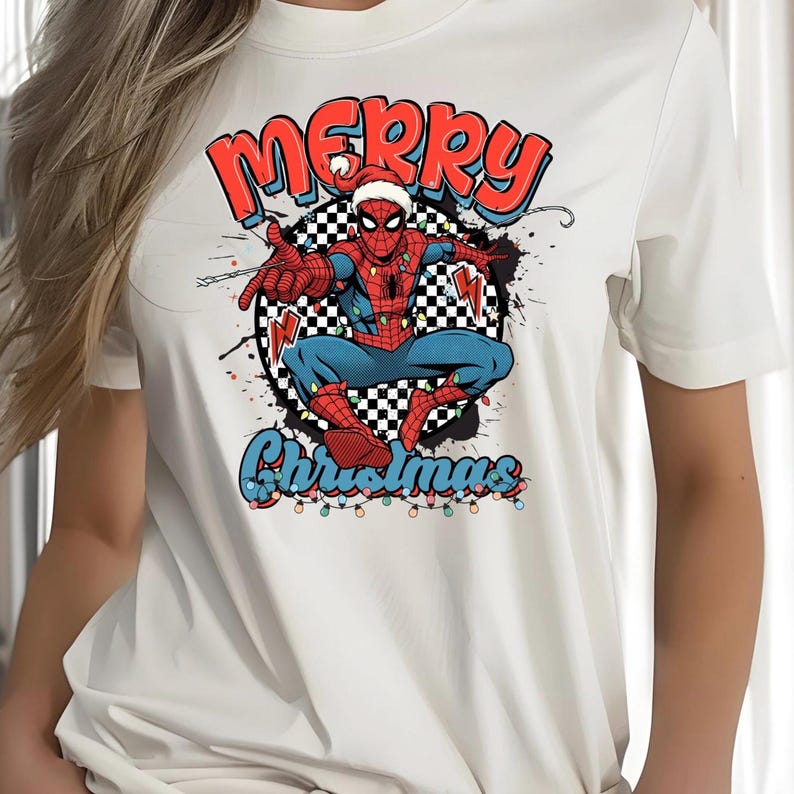 Puede incluir: Camiseta blanca con un gr&aacute;fico festivo de Spider-Man con gorro de Pap&aacute; Noel, las palabras "Merry Christmas" y luces navide&ntilde;as. El dise&ntilde;o incluye un fondo a cuadros. El superh&eacute;roe est&aacute; en una pose din&aacute;mica.