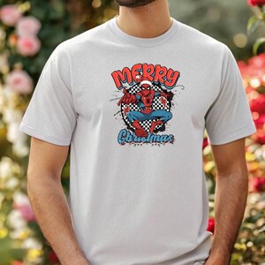 Puede incluir: Una camiseta gris claro con un dise&ntilde;o de Spider-Man con un gorro de Pap&aacute; Noel. El dise&ntilde;o incluye las palabras "MERRY" en rojo, "Christmas" en azul y un c&iacute;rculo a cuadros. El superh&eacute;roe est&aacute; en una pose din&aacute;mica.