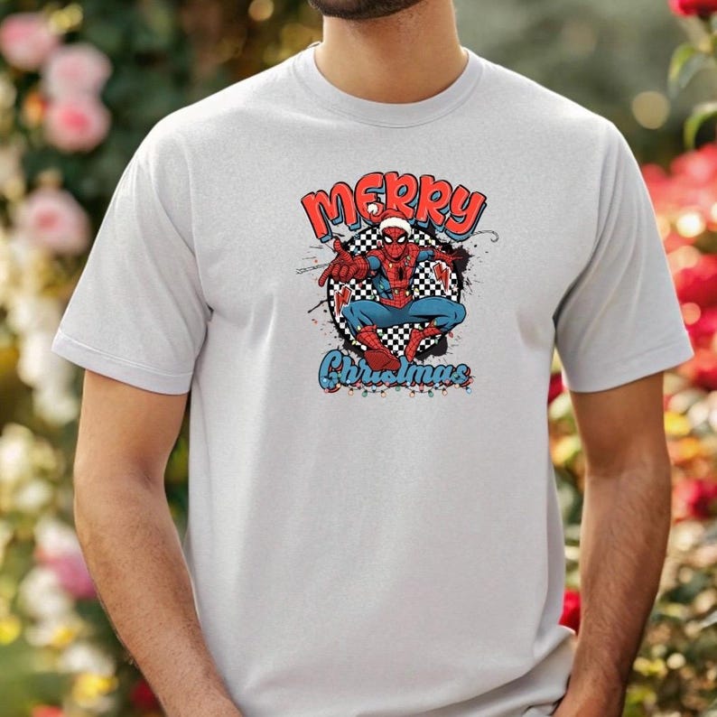 Puede incluir: Una camiseta gris claro con un dise&ntilde;o de Spider-Man con un gorro de Pap&aacute; Noel. El dise&ntilde;o incluye las palabras "MERRY" en rojo, "Christmas" en azul y un c&iacute;rculo a cuadros. El superh&eacute;roe est&aacute; en una pose din&aacute;mica.