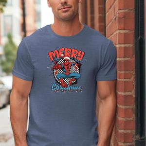 Puede incluir: Camiseta azul con un dise&ntilde;o de Spider-Man con gorro de Pap&aacute; Noel y la frase "Merry Christmas". El dise&ntilde;o incluye un fondo a cuadros y detalles festivos. La camiseta es de color azul liso.
