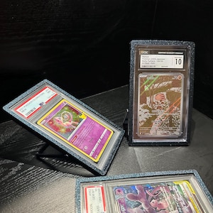 Op de afbeelding: Drie beoordeelde Pokémon-ruilkaarten in beschermende hoesjes. Eén kaart toont Mew, een andere Mewtwo en de derde een Japanse kaart. De hoesjes worden op een donkere ondergrond gepresenteerd, waarbij de details van de kaarten worden getoond.