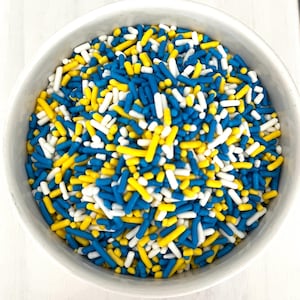 May include: A white bowl filled with blue, yellow, and white sprinkles. The sprinkles are long and thin, and they are perfect for decorating cakes and cupcakes.