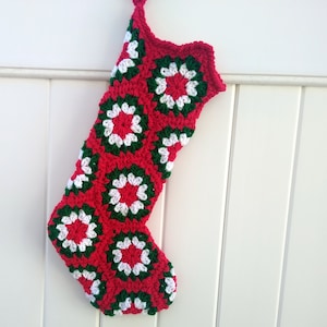 May include: A red, green, and white crocheted Christmas stocking with a traditional stocking shape. The stocking is made of granny squares with a white center and red and green borders.