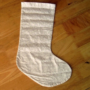 May include: A white stocking with a delicate floral pattern. The stocking is made of a soft, lightweight fabric and has a traditional Christmas stocking shape.