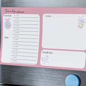 May include: A pink magnetic daily planner, 10 x 6 inches, with sections for schedule, to-do list, and doodles. Includes illustrations of an Easter egg and a bow. The schedule is divided into hourly slots from 6 AM to 9 PM.