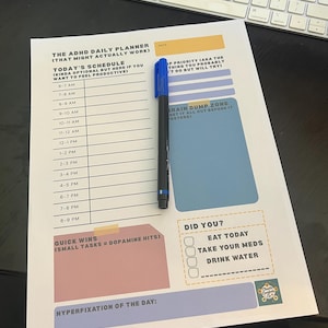 May include: A printed ADHD daily planner with a blue marker. The planner includes sections for scheduling, priorities, and quick wins. Text on the planner includes "Brain Dump Zone" and "Did You?" with checkboxes.
