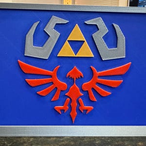 May include: A blue shield with a silver frame and accents, featuring a red and yellow emblem. The emblem includes a stylized bird and a yellow triangle. The shield is a decorative item.