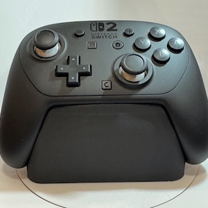 May include: A black Nintendo Switch Pro Controller with the Nintendo Switch logo. The controller has two analog sticks, a directional pad, and action buttons. It is designed for use with the Nintendo Switch console.