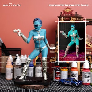 Könnte beinhalten: Handgefertigte, personalisierte Statue eines blauen Alien-Mädchens mit einer Strahlenpistole. Die Figur trägt einen silber-blauen Body, passende Stiefel und ein Visier. Der Sockel ist schwarz mit dem Text "BLUE ALIEN GIRL".