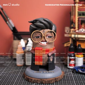 May include: A handcrafted personalized statue of a character with black hair, glasses, and a lightning bolt scar. The statue wears a scarf and a black robe. The base is gray with the name "Allie Potter" on it. The background includes paint bottles and brushes.