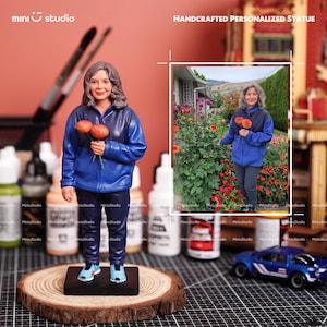 May include: A handcrafted personalized statue of a person wearing a blue jacket and dark pants, holding orange flowers. The statue is on a wooden base, with a miniature car and paint bottles in the background.