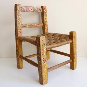May include: A small, hand-painted wooden chair with a woven seat. The chair features a yellow base with floral accents in pink, red, and green. The chair is approximately 24 inches tall.