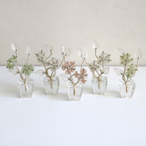 May include: Five miniature decorative floral arrangements in clear glass square vases. Each piece features delicate wire stems, translucent leaf accents, and clusters of small, rounded beads in shades of pale green, white, and soft pink.