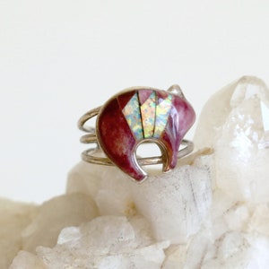 May include: A silver ring with a red and white bear design. The bear is made of inlaid stone and is set on a silver band.