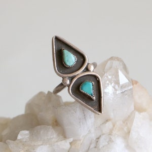 May include: A silver ring with two turquoise stones set in a triangular shape.
