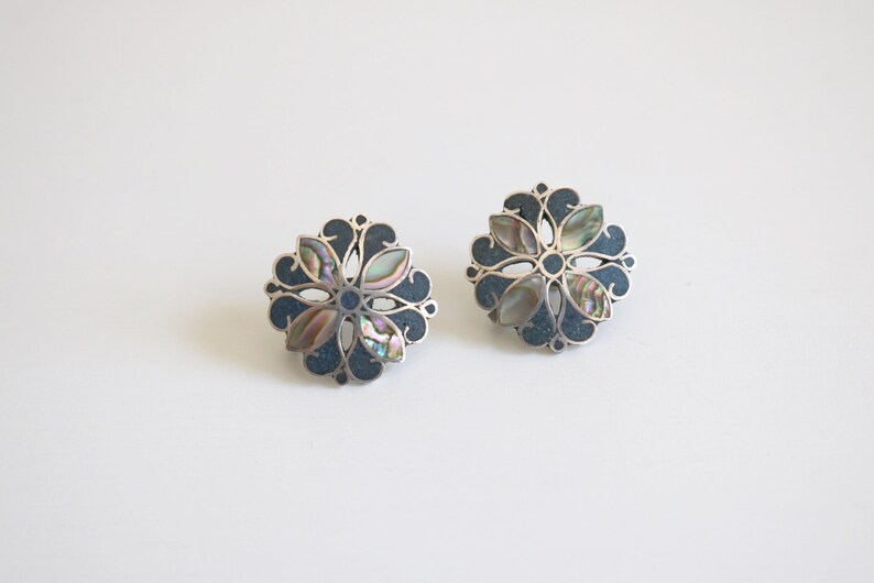 May include: A pair of silver earrings with a blue and iridescent abalone shell flower design.