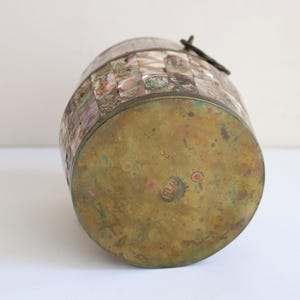 May include: A vintage barrel-shaped container with a brass base and lid. The body is adorned with a mosaic of iridescent, rectangular tiles in shades of pink, white, and gray. A dark metal clasp secures the lid.