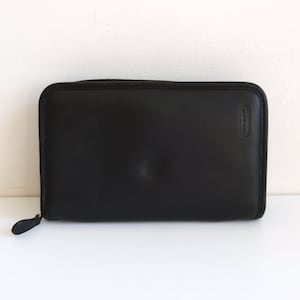 Cartera de mano con cremallera y diseño de agenda de Coach, de cuero negro